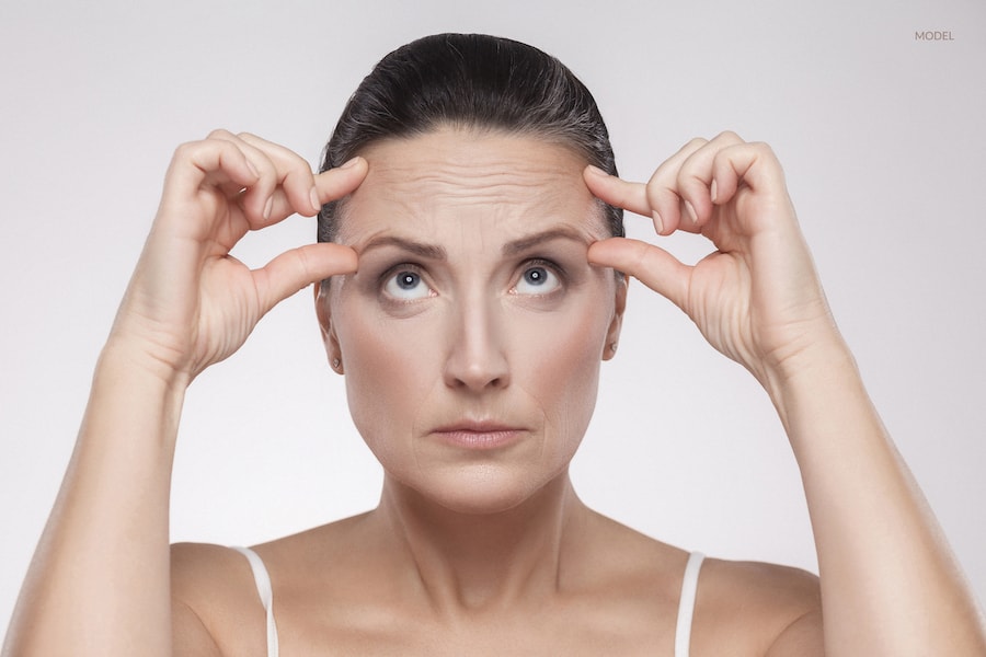 Woman scrunching up the skin on her forehead to show the improvement that would be offered with a brow lift.