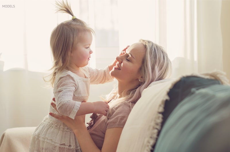 Toddler touching her mother's face as they sit on the couch.